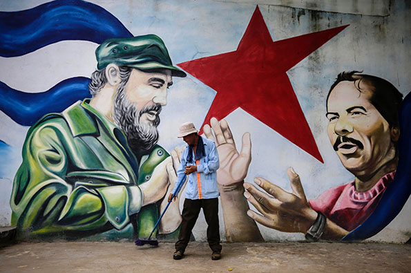 TOPSHOT - A municipal worker sweeps the floor in front of a mural depicting Cuban revolutionary leader Fidel Castro (L) and Nicaraguan President Daniel Ortega at Cuba square in Managua on November 26, 2016, the day after Castro died. Cuban revolutionary leader Fidel Castro has died aged 90, prompting mixed grief and joy Saturday along with international tributes for the man whose iron-fisted rule defied the United States for half a century. / AFP PHOTO / INTI OCONINTI OCON/AFP/Getty Images